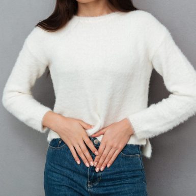 Close-up photo of depressed young woman with abdominal pain, looking at camera, isolated over gray background